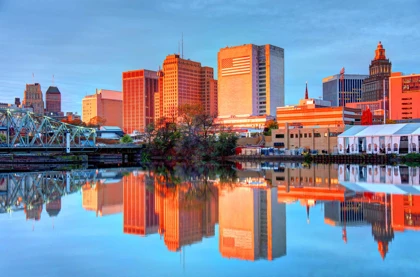 Downtown Newark skyline reflected in the Passaic River at sunrise, with modern and historic buildings