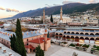 Historic mosque and bustling bazaar district in Bursa, Turkey, with mountain backdrop at sunset