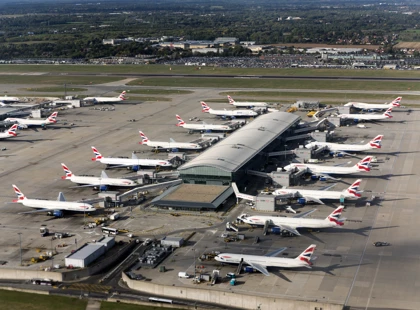 An aerial view of Heathrow Airport showing multiple British Airways planes parked at gates around a large terminal building