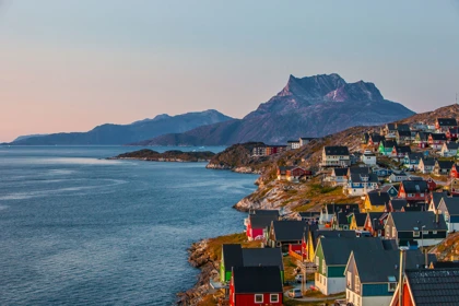 Colorful houses along the rocky coastline of Nuuk, Greenland, with mountains and the sea in the background at sunset
