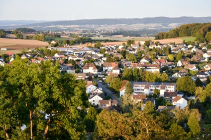 Aerial view of Gudensberg, Germany, showcasing a small town with red-roofed houses, green landscapes, and rolling hills in the background
