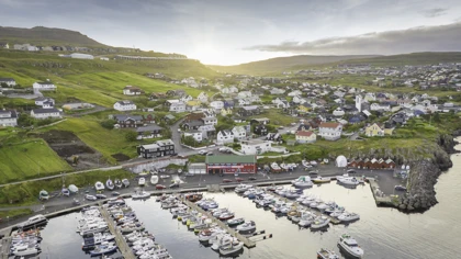 Scenic view of a harbor in the Faroe Islands with colorful houses on green hills at sunrise