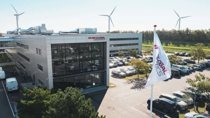Scan Global Logistics headquarters building with company flag, parking lot, and wind turbines in the background