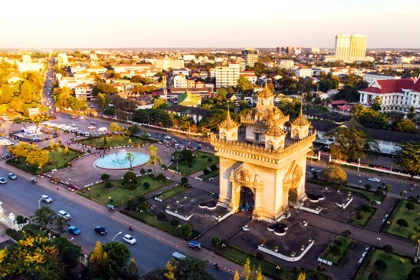 Patuxai Monument in Vientiane, Laos, surrounded by gardens and city buildings at sunset