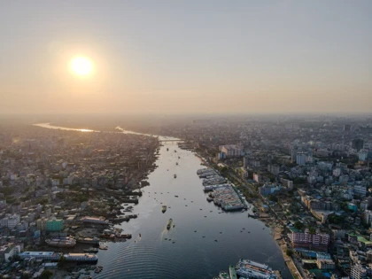Aerial view of Dhaka city at sunset, with the Buriganga River lined with boats and bustling urban areas