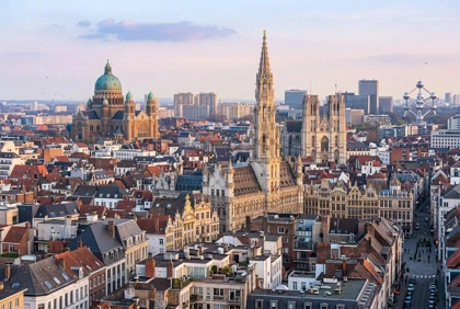Panoramic cityscape of Brussels at sunset, with historic church towers rising above dense rooftops and urban buildings