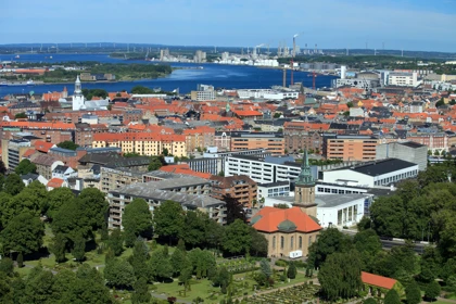 Panoramic view of Aalborg, Denmark, showcasing red-roofed buildings, a church with a green spire, and an industrial harbor in the background
