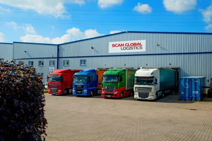 Scan Global Logistics trucks in various colors parked outside the warehouse, with a blue sky and company sign above