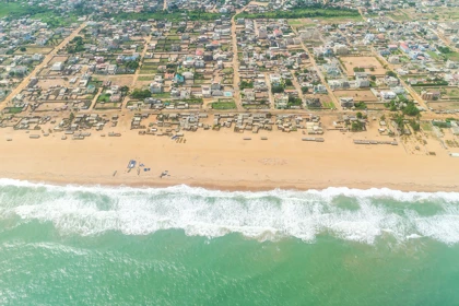 Aerial view of Cotonou, Benin, showing a sandy beach, ocean waves, and urban buildings along the coastline