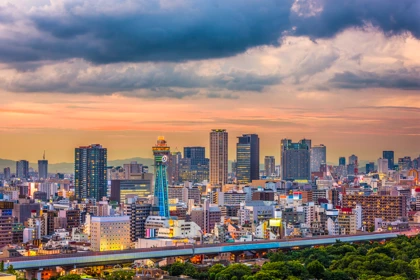 Osaka skyline at sunset, featuring Tsutenkaku Tower illuminated among modern skyscrapers and city buildings