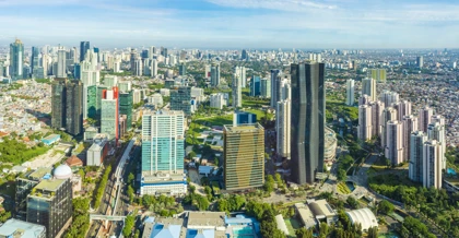 Panoramic aerial view of Jakarta's modern skyline with skyscrapers, green spaces, and urban infrastructure under a clear sky
