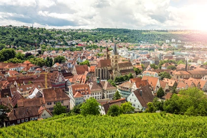 Aerial view of Stuttgart, Germany, featuring historic buildings, vineyards, and green hills under a partly cloudy sky