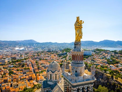 Panoramic view of Marseille, France, featuring the golden statue of Notre-Dame de la Garde overlooking the city and coastline