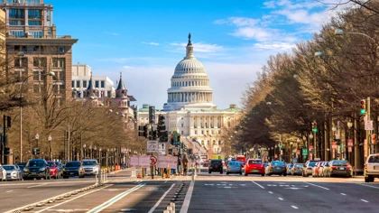 View of the U.S. Capitol building from a busy street in Washington, D.C., lined with trees and cars
