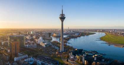 Aerial view of Düsseldorf, Germany, featuring the Rheinturm tower, modern architecture, and the Rhine River at sunset
