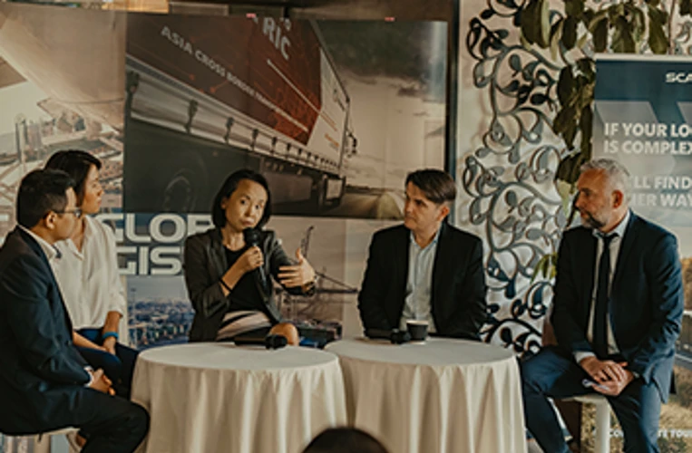 Panel discussion with five professionals seated around round tables, one woman speaking into a microphone, with SGL banners in the background