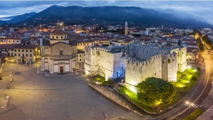 Evening aerial view of Prato, Italy, showcasing the illuminated Prato Cathedral and Castello dell'Imperatore