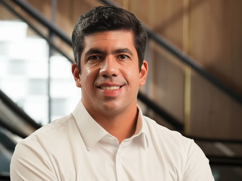 Gabriel Carvalho smiling confidently in a white shirt, with modern architectural elements in the background.