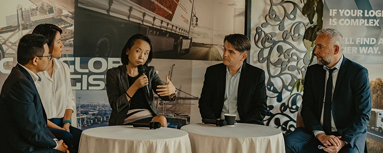 Panel discussion with five professionals seated around round tables, one woman speaking into a microphone, with SGL banners in the background