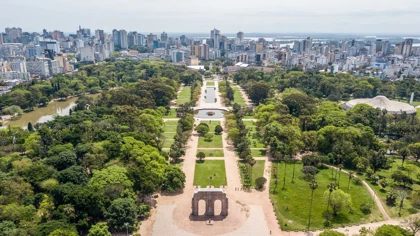 Aerial view of Redemption Park (Parque Farroupilha) in Porto Alegre, Brazil, with green trees, pathways, and a city skyline in the background.