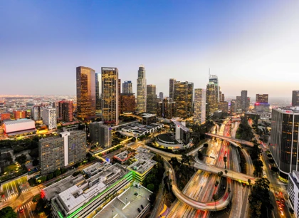 Downtown Los Angeles skyline at dusk with illuminated skyscrapers and busy highways filled with light trails