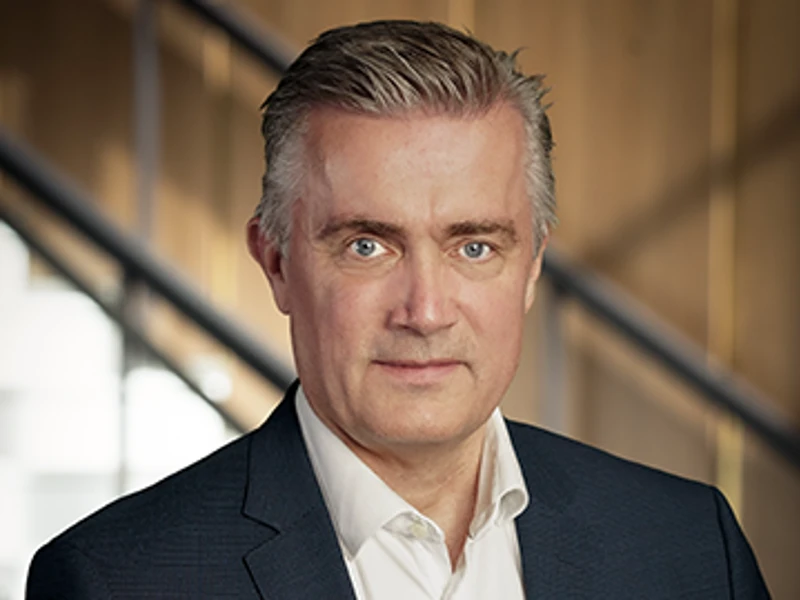 Steen Søgaard in a professional portrait, wearing a dark suit and white shirt, posing confidently against a modern office background