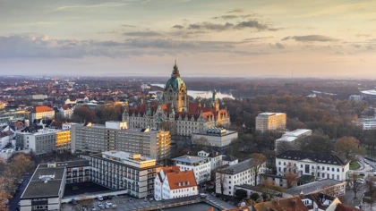 Aerial view of Hanover, Germany, featuring the New Town Hall surrounded by city buildings and autumn trees at sunset