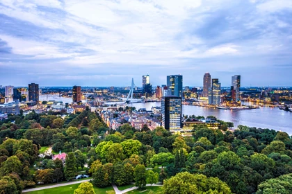 Rotterdam skyline at twilight, featuring the Erasmus Bridge, modern skyscrapers, and a lush green park in the foreground